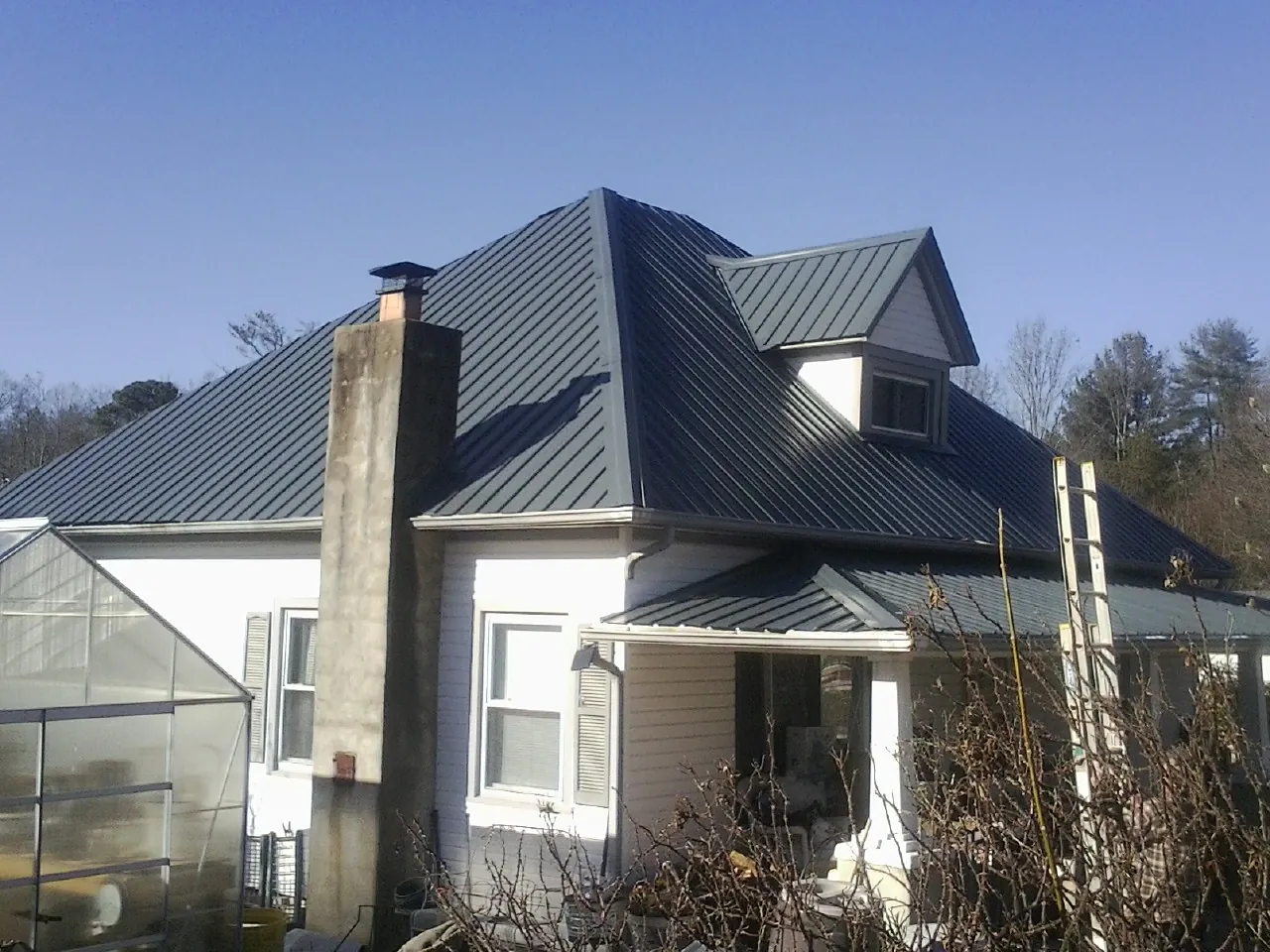 Dark blue standing seam metal roof on a white farmhouse with dormer — Slate & Tile Roof Repair by Roofing Brothers in Bassfield