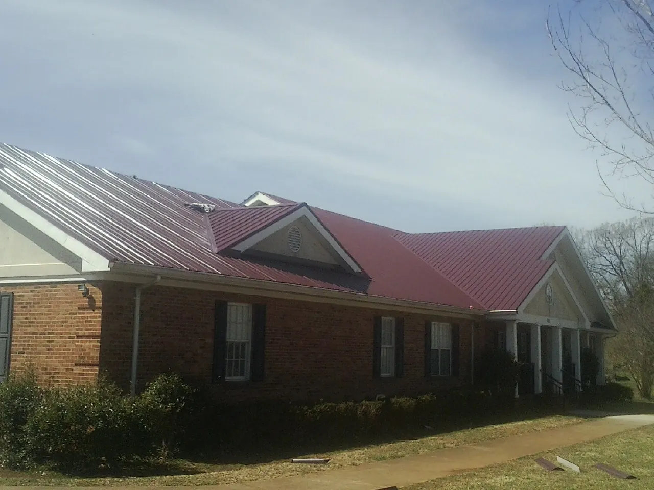 Red metal roof with gabled entries on a long brick building, from a Hail Damage Roof Repair job in Bassfield