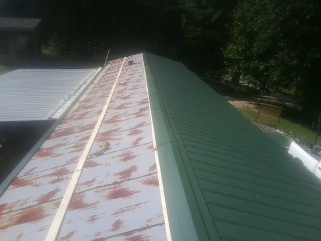 Old rusted panels beside newly installed green metal roofing — Wind Damage Roof Repair by Roofing Brothers in Bassfield