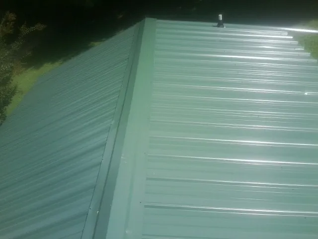 New green metal panels meeting at the ridge of a roof — Flat Roof Repair work by our crew in Bassfield