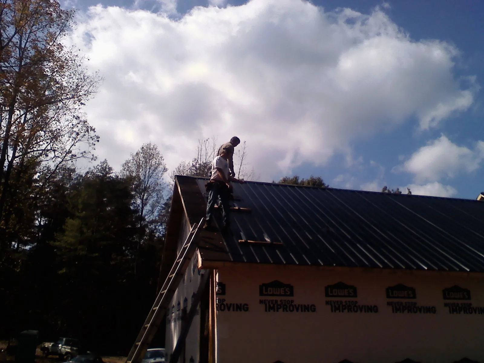 Roofer fastening dark metal panels high against a cloudy sky, from a Roof Inspection job in Bassfield