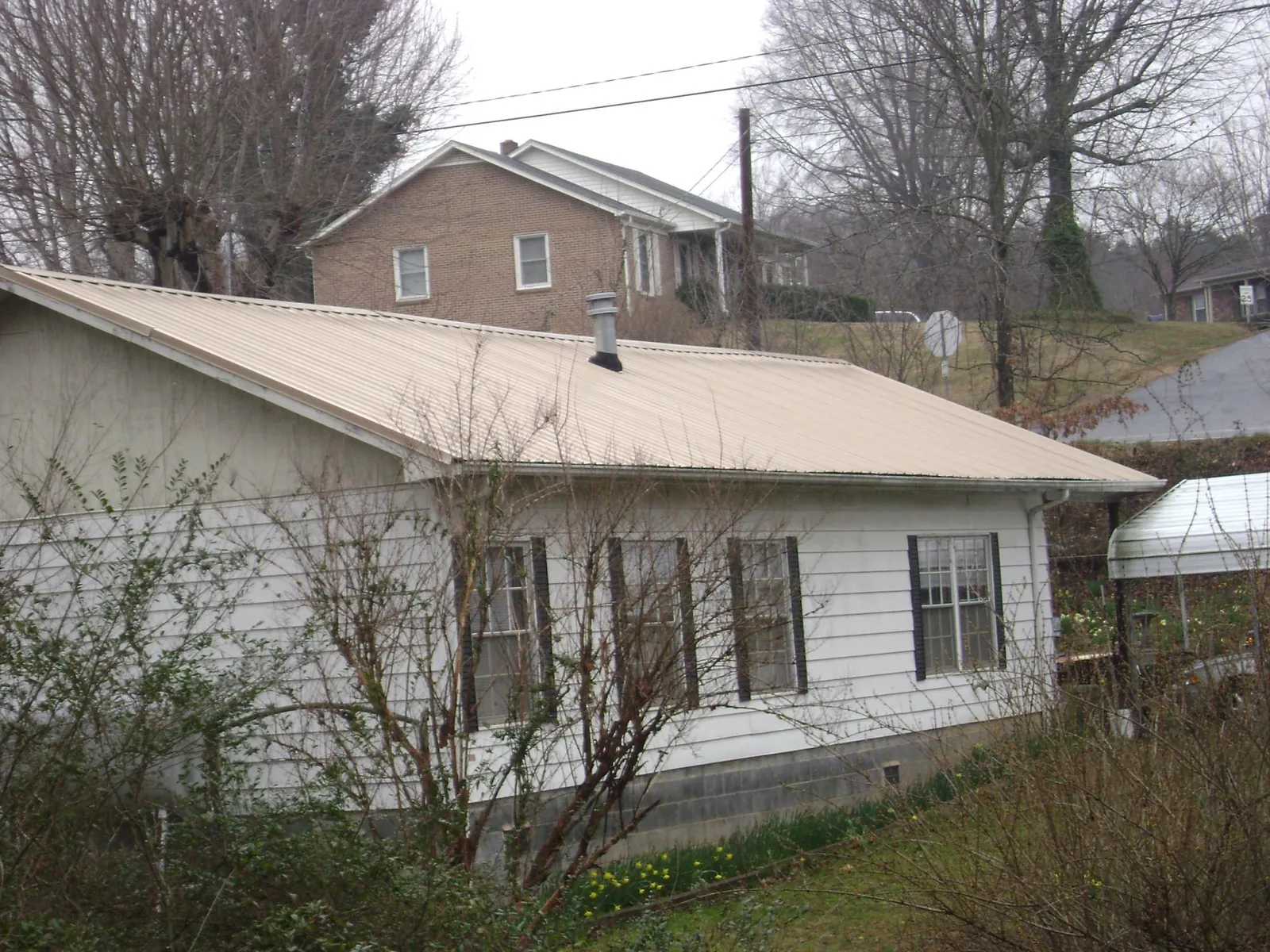 Tan metal roof on a white sided house set into a hillside — Commercial Roofing by Roofing Brothers in Bassfield