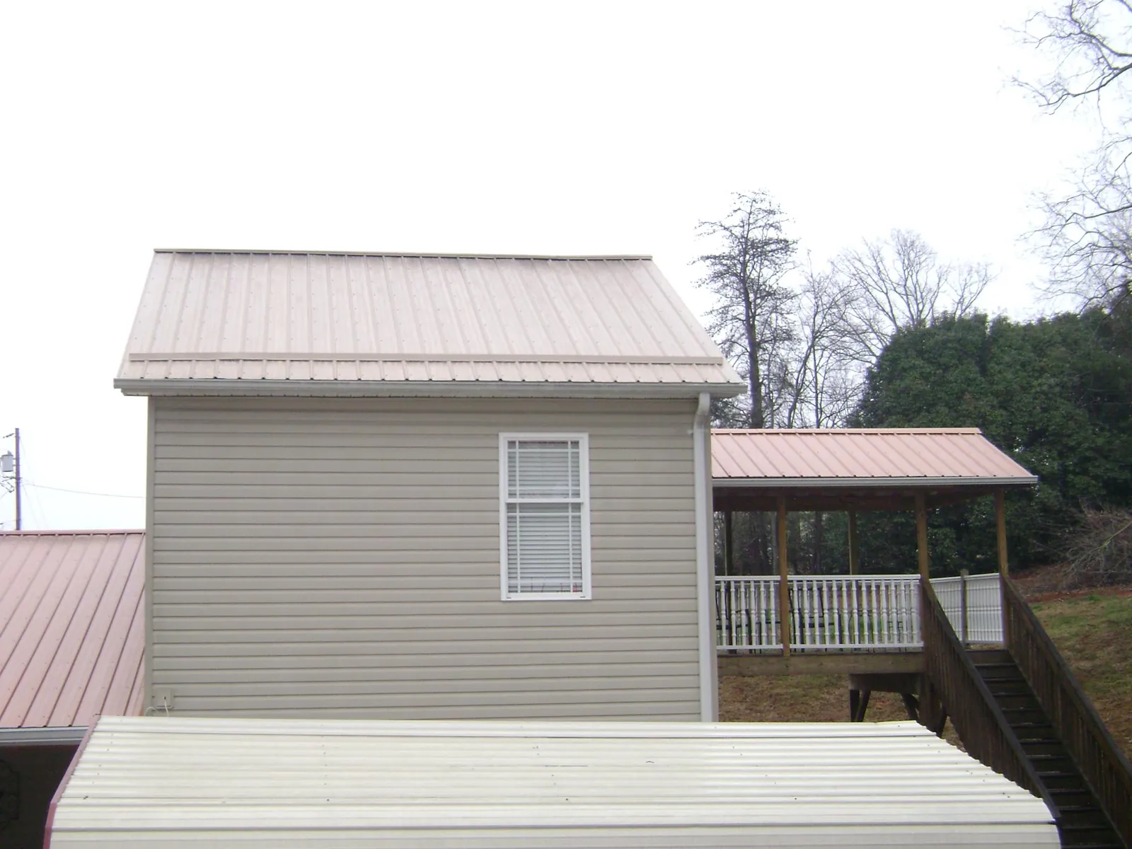 Tan metal roofs on a two story addition and attached porch, from a Roof Replacement job in Bassfield
